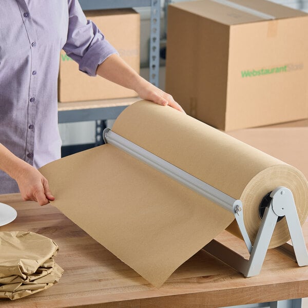 A large roll of natural kraft packing paper on a metal dispenser being pulled for use.