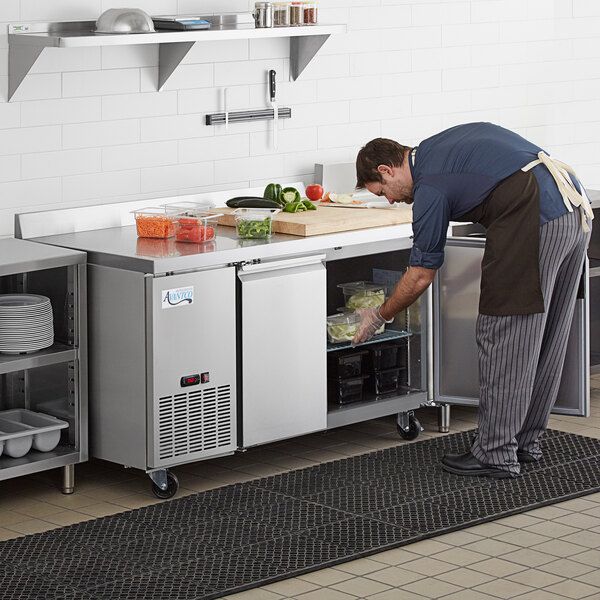 An aproned man preparing food on a stainless steel worktop refrigerator.