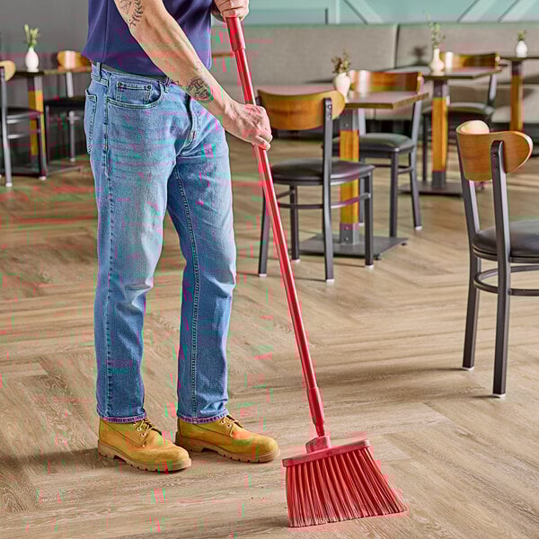 A man using a Carlisle Sparta Duo-Sweep broom with red flagged bristles to sweep the floor.