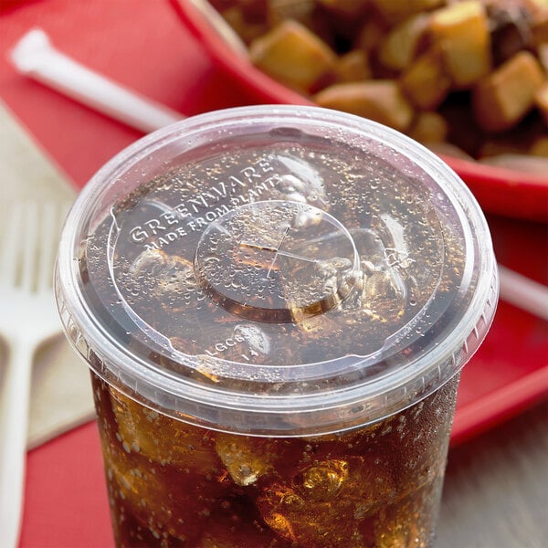 A Fabri-Kal Greenware plastic lid with a straw slot on a plastic cup with a soda in it.