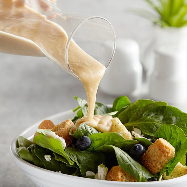 A person pouring AAK Select Recipe Honey Mustard Dressing into a bowl of salad.