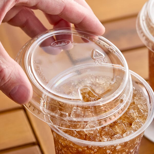 A clear plastic strawless lid being placed on a cold beverage cup filled with ice and soda.