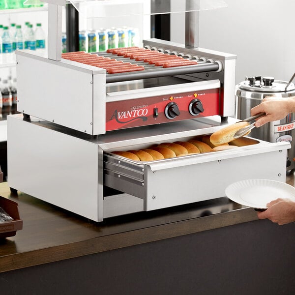 A woman using an Avantco stainless steel bun warmer to heat hot dog buns.