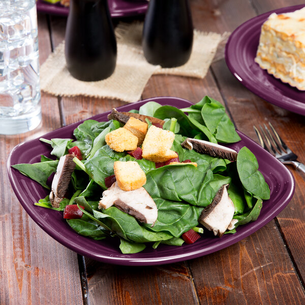A mulberry Fiesta luncheon plate with salad, meat, and croutons on it.