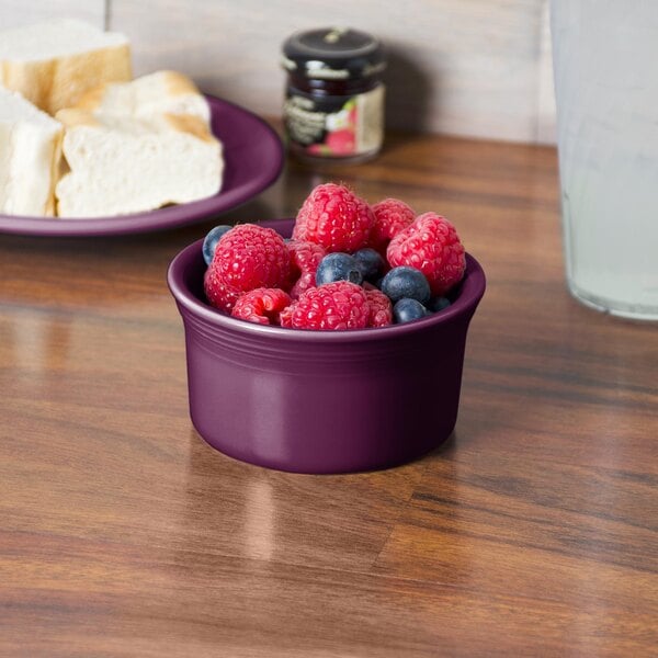 A Fiesta Mulberry china ramekin filled with raspberries on a table with bread.