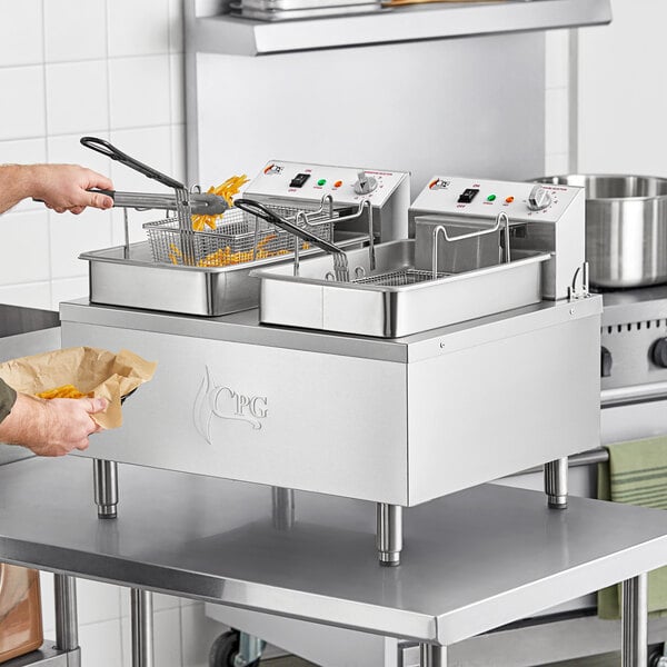 A woman using a Cooking Performance Group electric countertop fryer to cook french fries on a school kitchen counter.