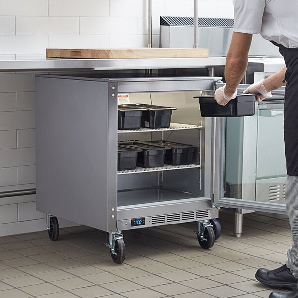 A man in a white shirt and black apron opening the glass door of a Beverage-Air undercounter freezer.