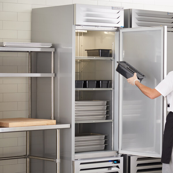 A man in a white apron opening the solid door of a Beverage-Air reach-in freezer.