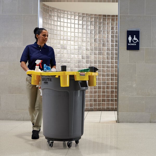 A woman standing next to a Rubbermaid BRUTE trash can with dolly.