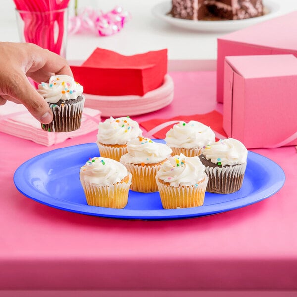 A hand holding a cupcake on a peacock blue oval melamine platter.