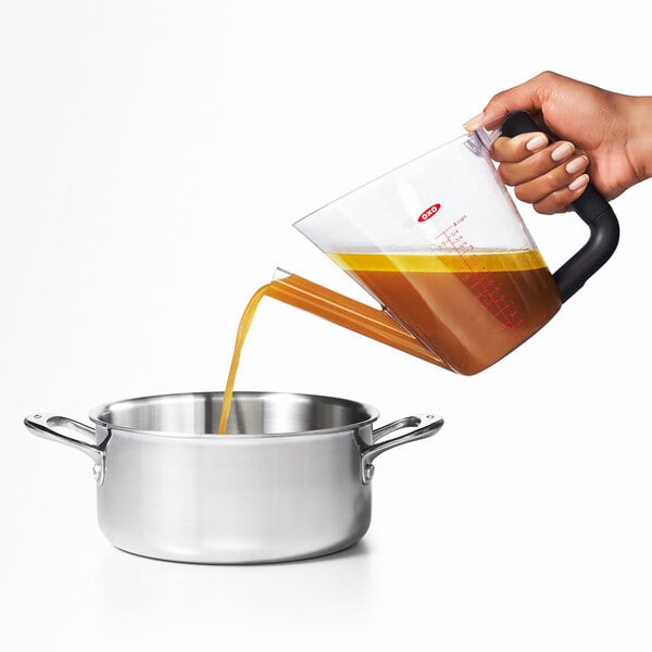 A hand using an OXO Good Grips fat separator to pour brown liquid into a pot.
