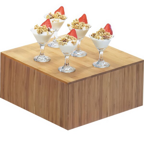 A Cal-Mil bamboo square riser with glasses of desserts inside on a wooden surface.