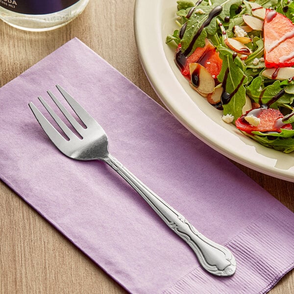 A Choice Bethany stainless steel salad fork on a napkin next to a plate of salad.