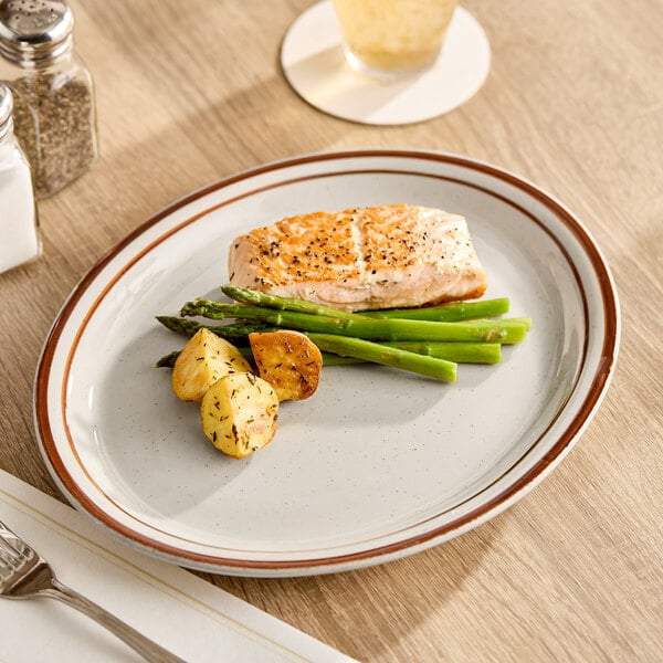 A Libbey narrow rim stoneware platter with food, a piece of fish, and asparagus on a table.