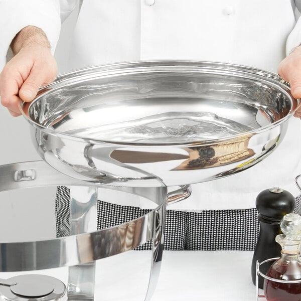 A chef holding a stainless steel water pan for a chafer.
