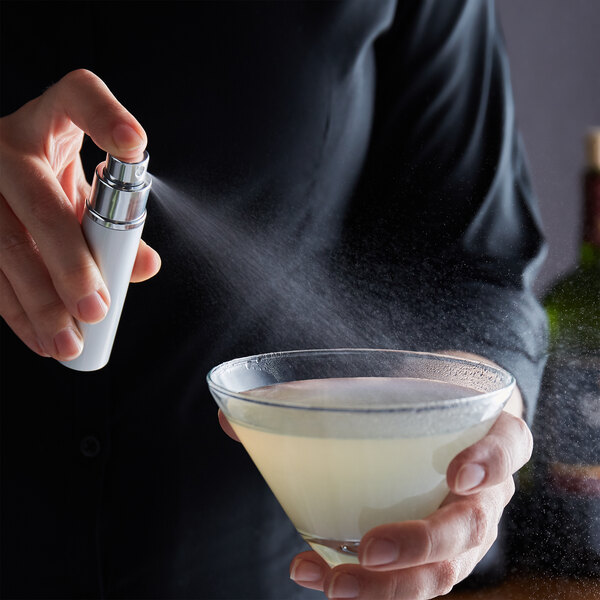 A person using a Franmara Martini Atomizer to spray liquid into a glass.