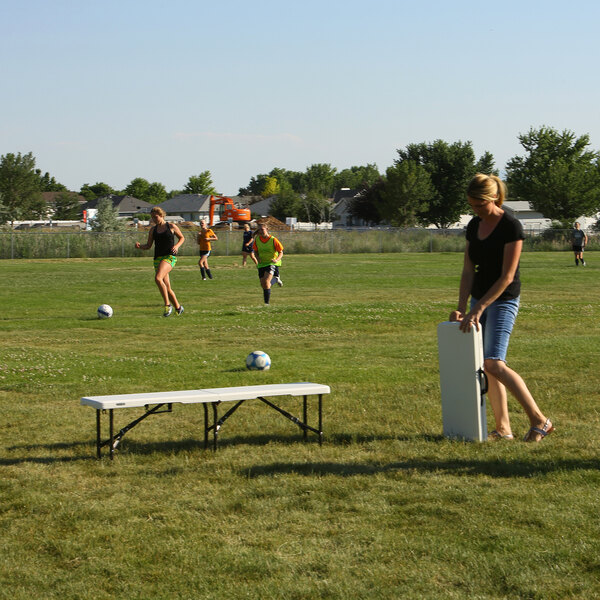 A white Lifetime 5' Bi-Fold Bench with a gray steel frame on a grassy field.