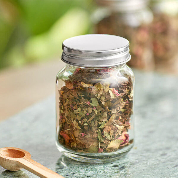 An Acopa Rustic Charm mini mason jar filled with dried herbs with a wooden spoon in it.