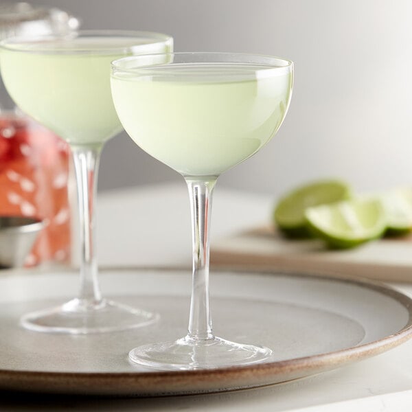 A pair of Arcoroc coupe cocktail glasses filled with green drinks on a plate.