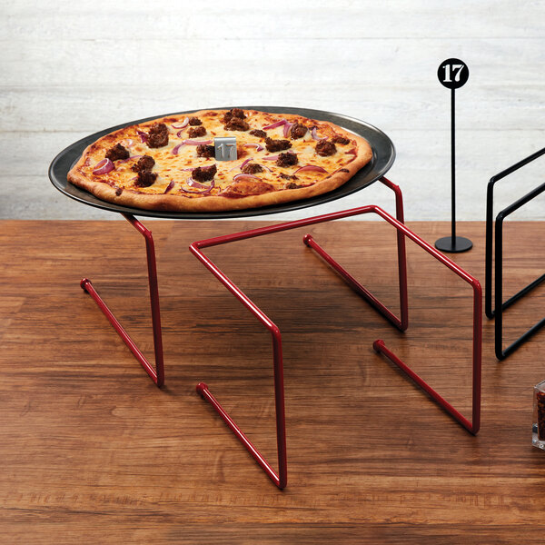 An American Metalcraft red rubberized pizza stand holding a pizza on a table.