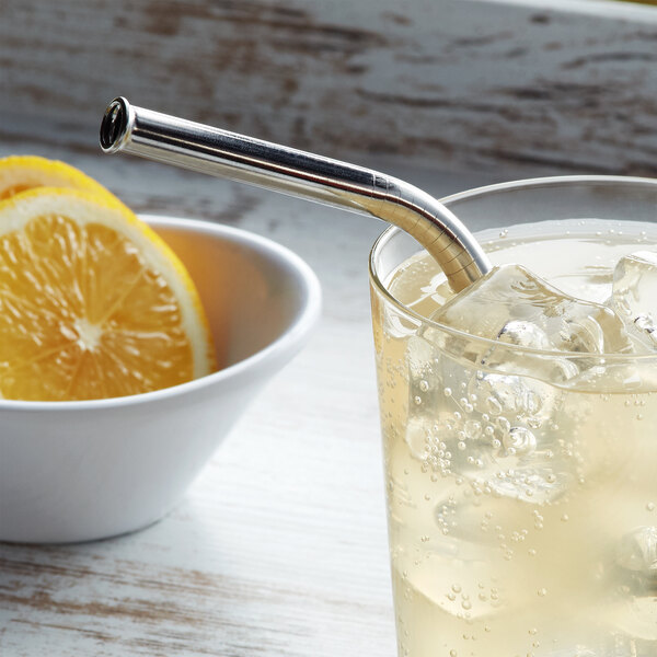A glass of liquid with ice and a Barfly stainless steel straw with a lemon slice.