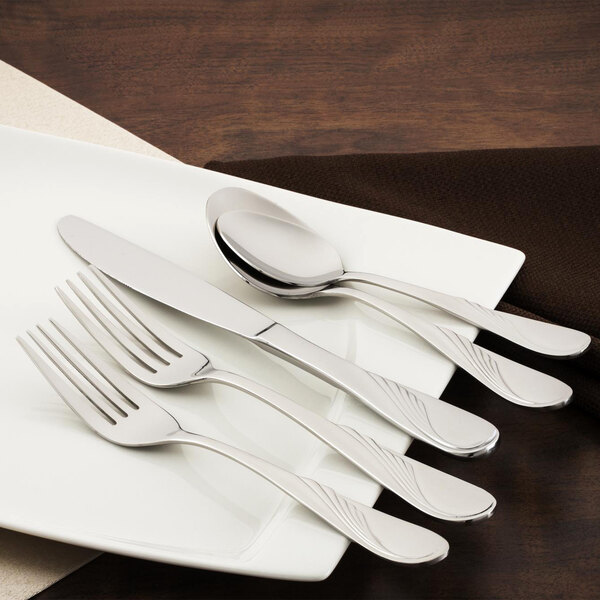 A white plate with a Walco Goddess stainless steel dinner knife and spoon on it.