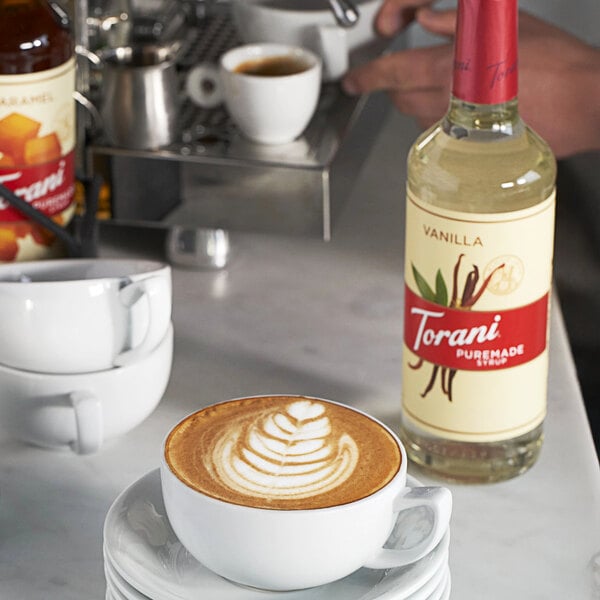 A close-up of a white cup of coffee with Torani Puremade Vanilla syrup on the table.