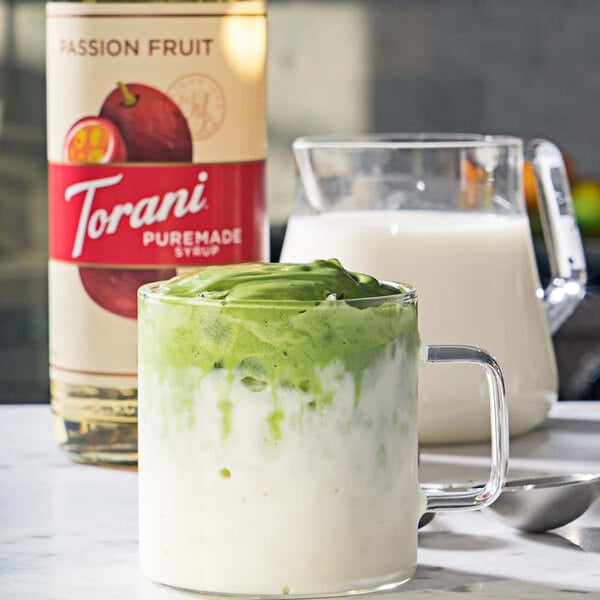 A glass of green and white liquid next to a bottle of Torani Puremade Passion Fruit Flavoring Syrup.
