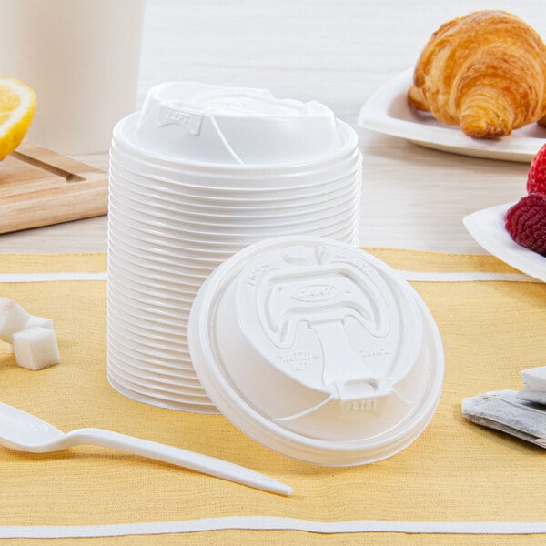 A white plastic lid with a reclosable tab on a stack of white plastic cups.