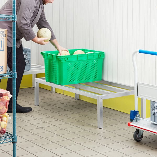 A man in a warehouse using a Regency aluminum dunnage rack to hold green plastic bins of fruit.