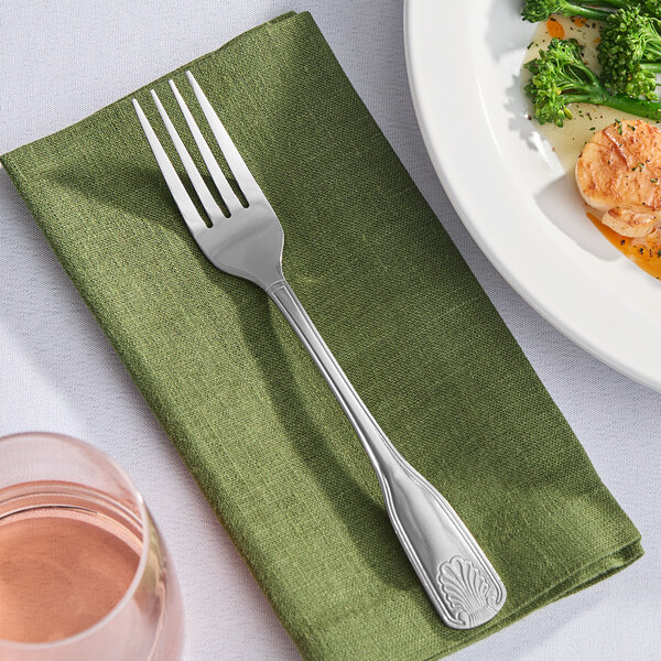 A Libbey stainless steel dinner fork on a green napkin next to a plate of food.