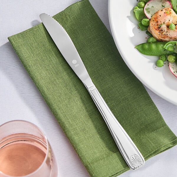A Libbey stainless steel dinner knife on a green napkin next to a plate of food.