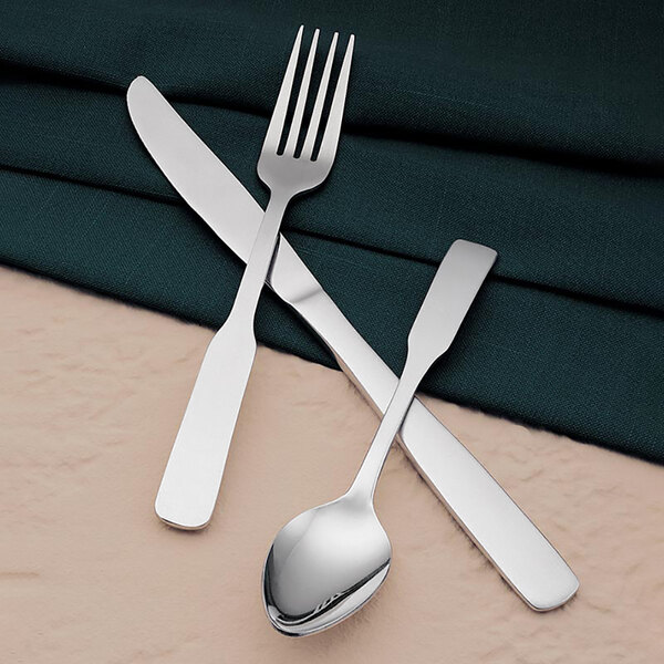 A Libbey stainless steel dessert spoon and knife on a cloth napkin.