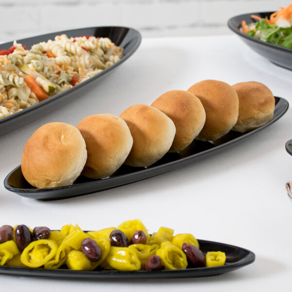 A black oval melamine platter on a table with several plates of food and a bowl of salad.