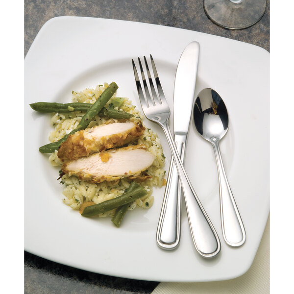 A close-up of a Libbey stainless steel demitasse spoon and fork on a plate of food.