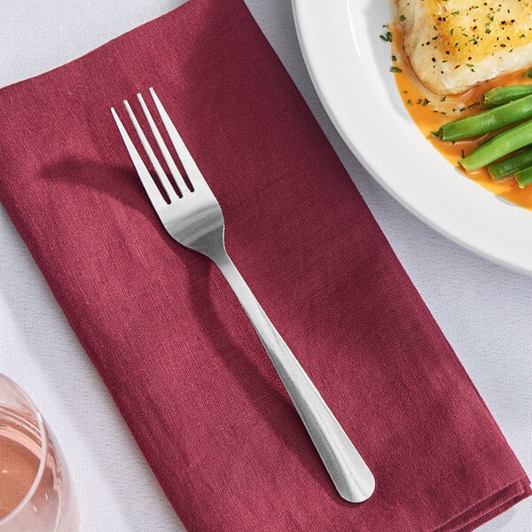 A Libbey Windsor stainless steel dinner fork on a red napkin next to a plate of food.