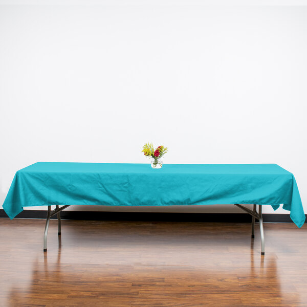 A table with a teal Intedge tablecloth and a bouquet of flowers on it.