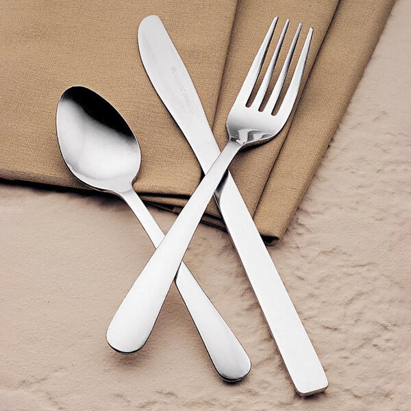 A Libbey stainless steel dinner knife on a napkin with a spoon and fork.