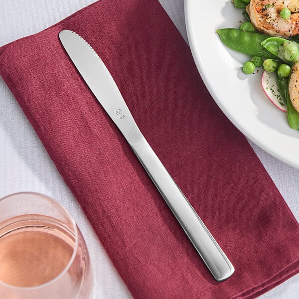 A Libbey Windsor stainless steel dinner knife on a red napkin next to a plate of food.