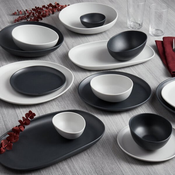 A dark gray irregular oval melamine plate on a white table with a black bowl on it.