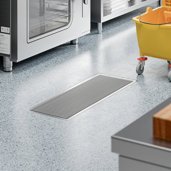A 12-inch by 36-inch stainless steel floor trough with a grate, installed in a commercial kitchen floor.