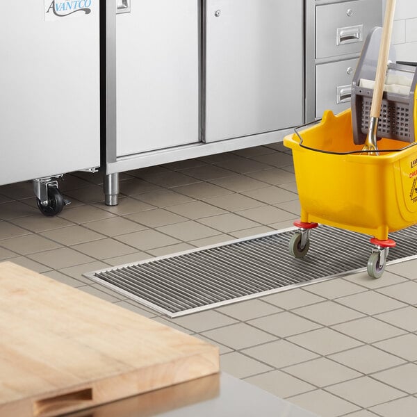 A yellow bucket with a mop in a kitchen floor trough.