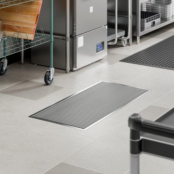 A rectangular stainless steel floor trough with a grate, installed in a commercial kitchen setting.