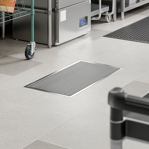 An 18 inch by 36 inch stainless steel floor trough with a grate, installed in a commercial kitchen floor.