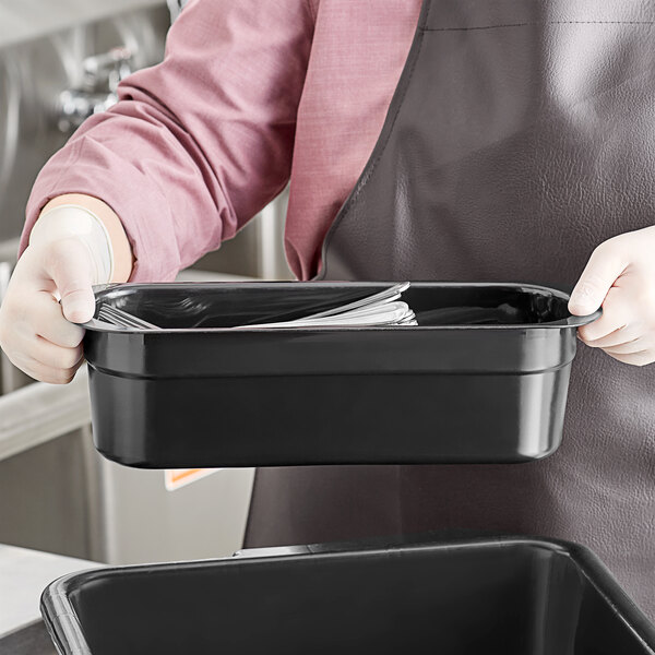 A person in an apron holding a black Cambro cutlery box on a counter.