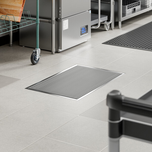A rectangular 24 x 36 inch stainless steel floor trough with a grate, installed in a commercial kitchen floor.