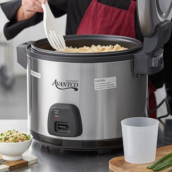 A woman using an Avantco 60 cup rice cooker to make rice in a professional kitchen.