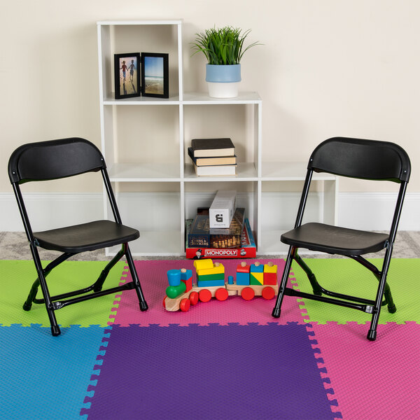 Two black Flash Furniture kids plastic folding chairs on a colorful mat.