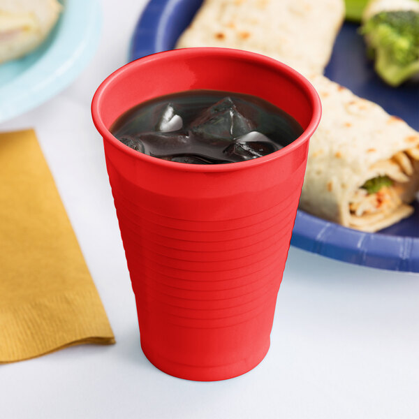 A Classic Red Plastic Cup with ice in it next to a plate of food.