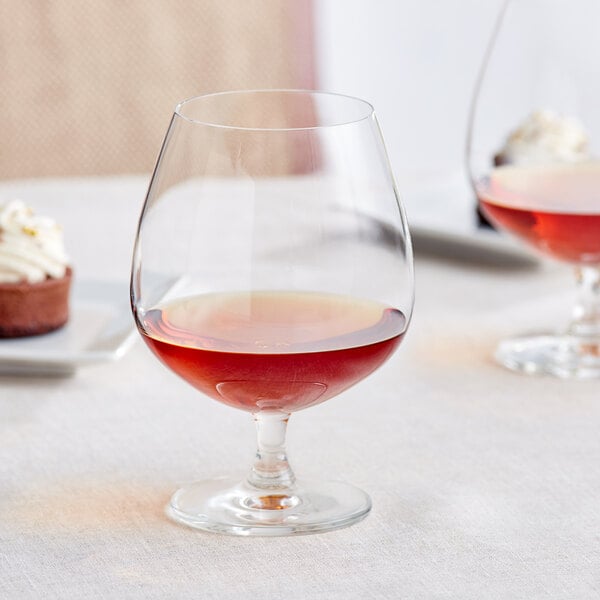 A table with a glass of brown liquid and a glass of wine.